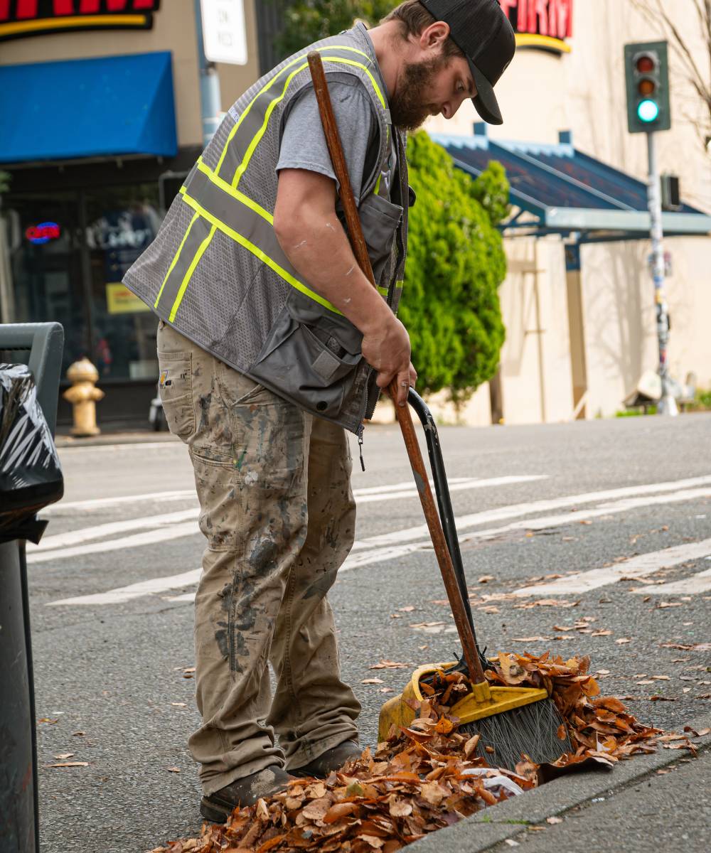 A Cultivator sweeping fallen leaves from a storm drain on a city street.